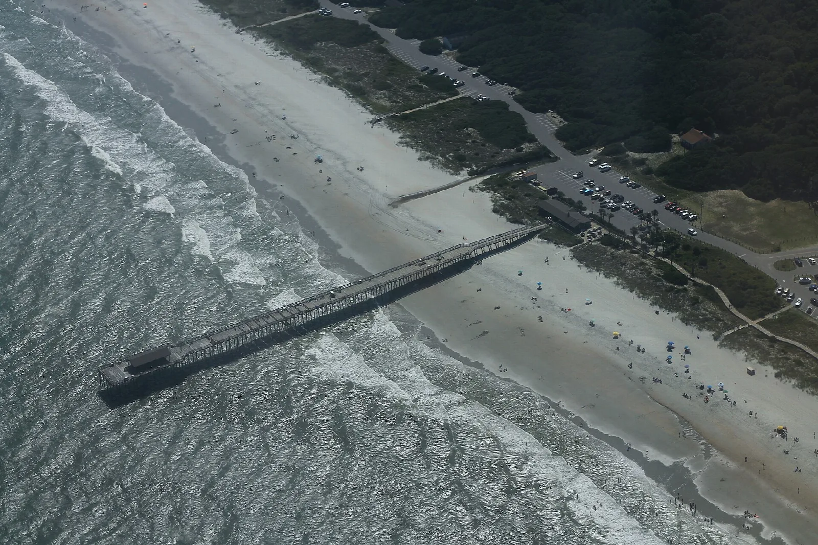Aerial view of a fishing pier reaching into the surf beside a sandy beach