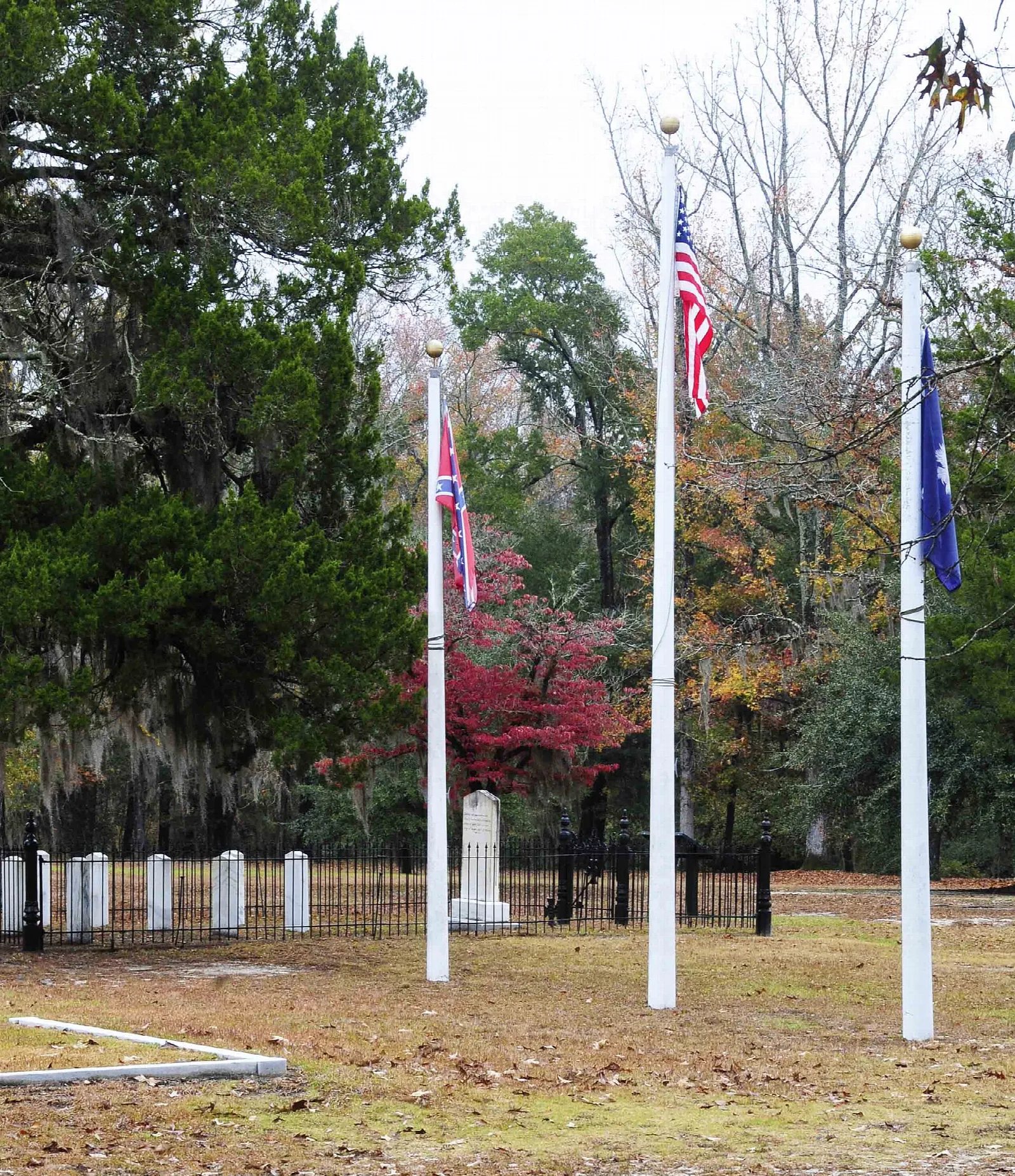 Flagpoles and rows of white headstones in a clearing among trees