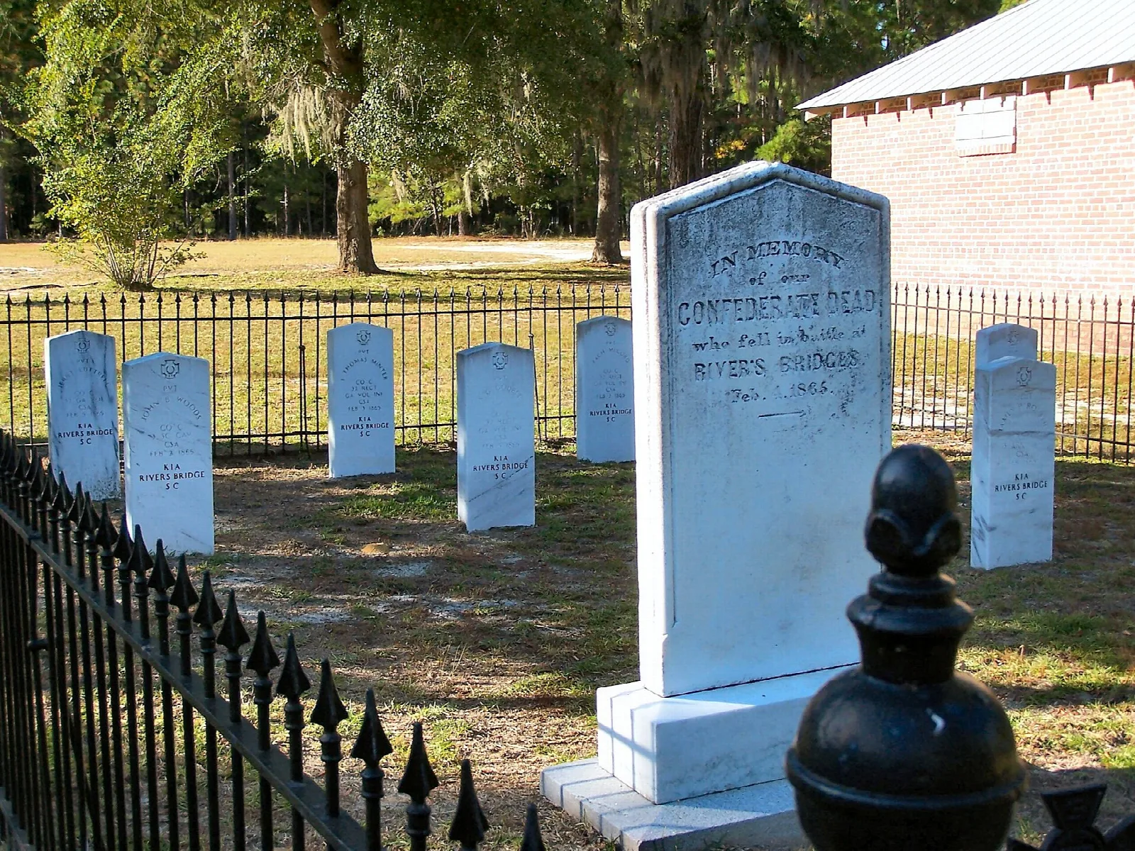 White headstones behind an iron fence, with a tall marker in front