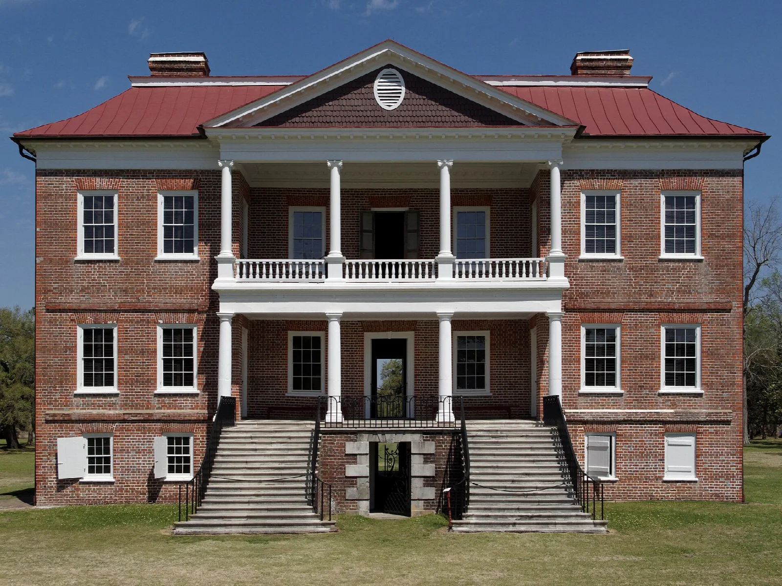 Rear of a red brick mansion with a white columned porch and stone steps