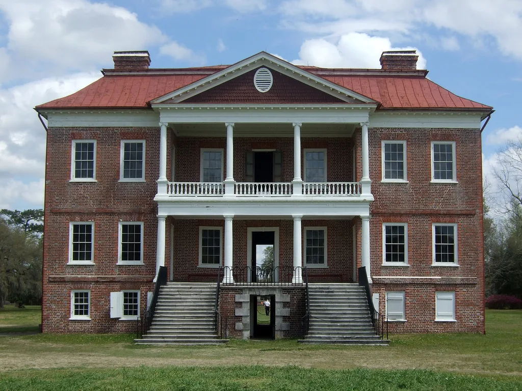 Two-story red brick house with a double porch and front stairs on a green lawn