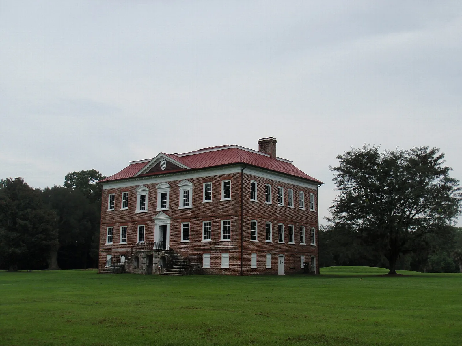 Red brick house with a red roof across a wide lawn under gray sky