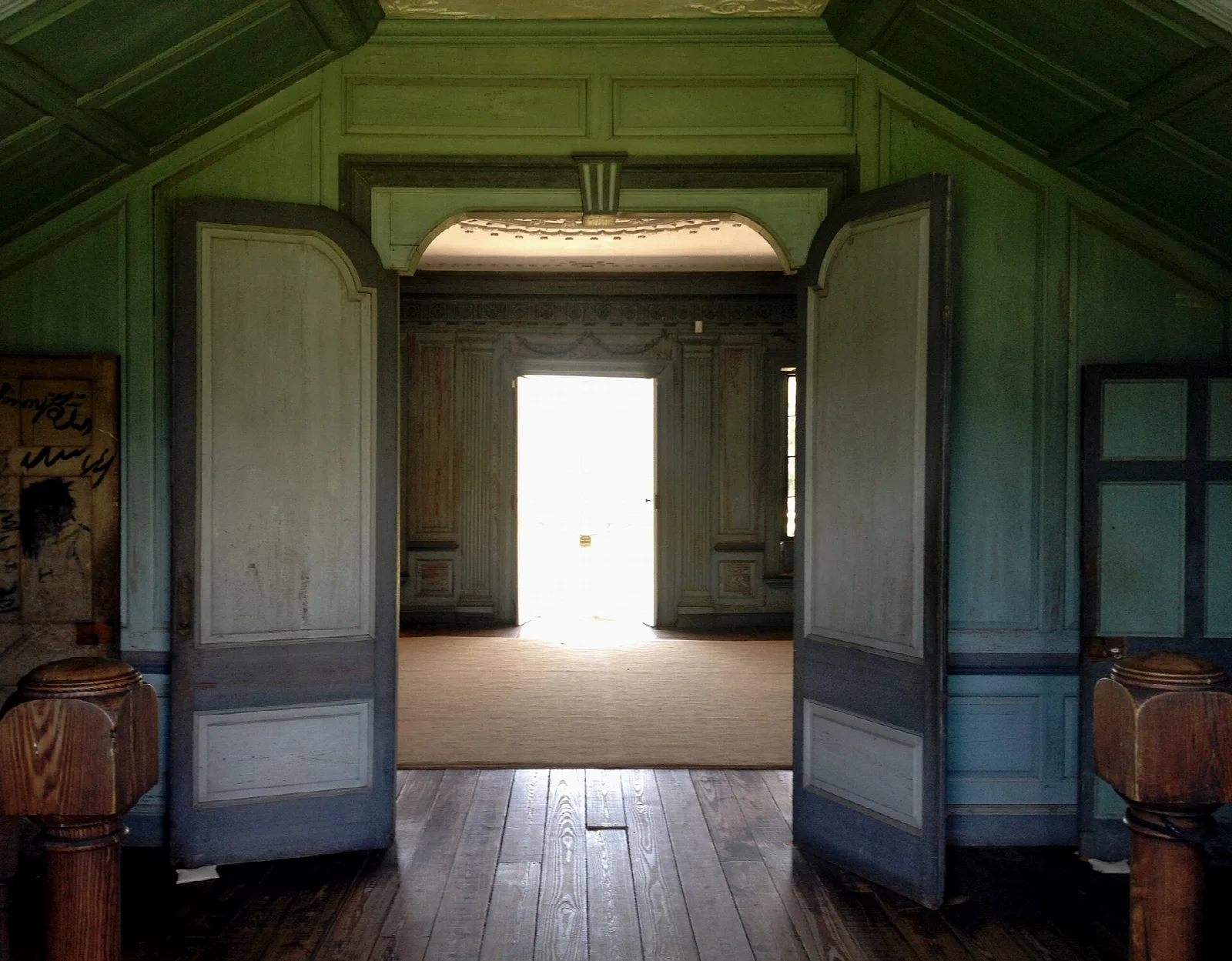 Open double doors looking through a green-painted room to bright daylight