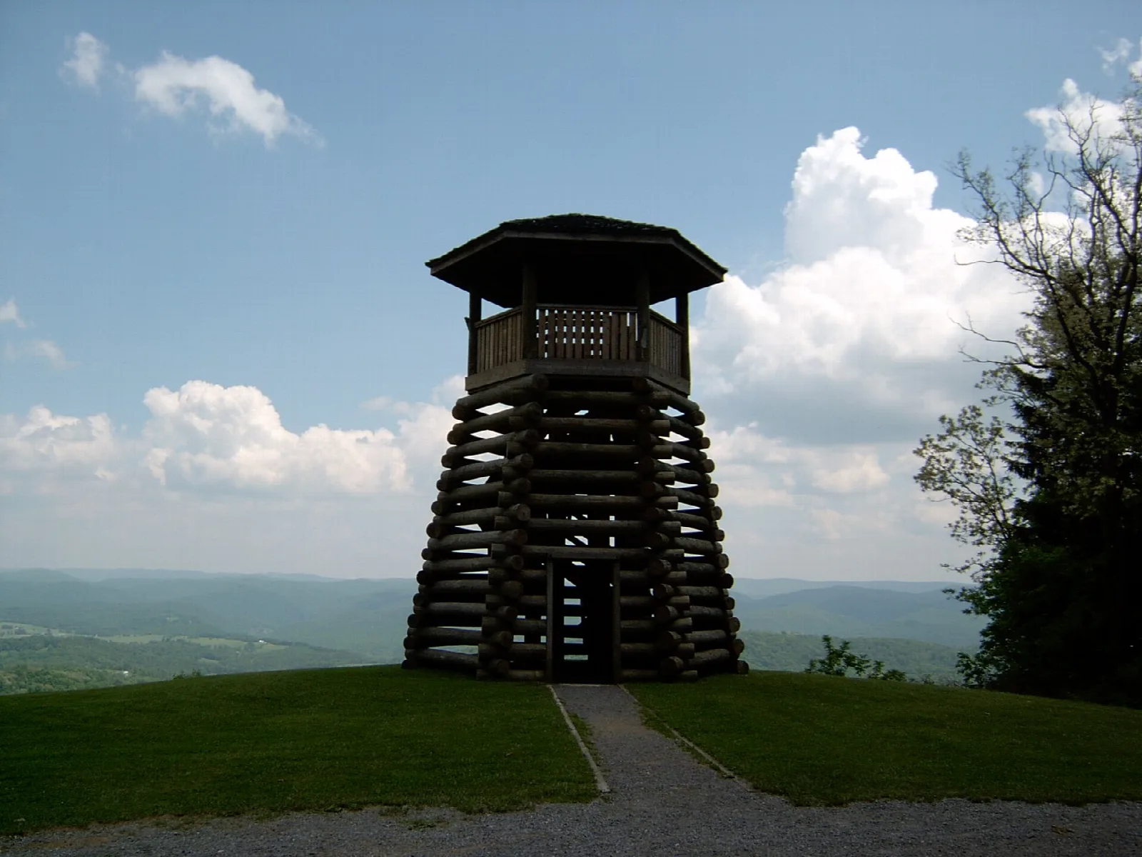 Log observation tower on a grassy hilltop under blue sky with clouds