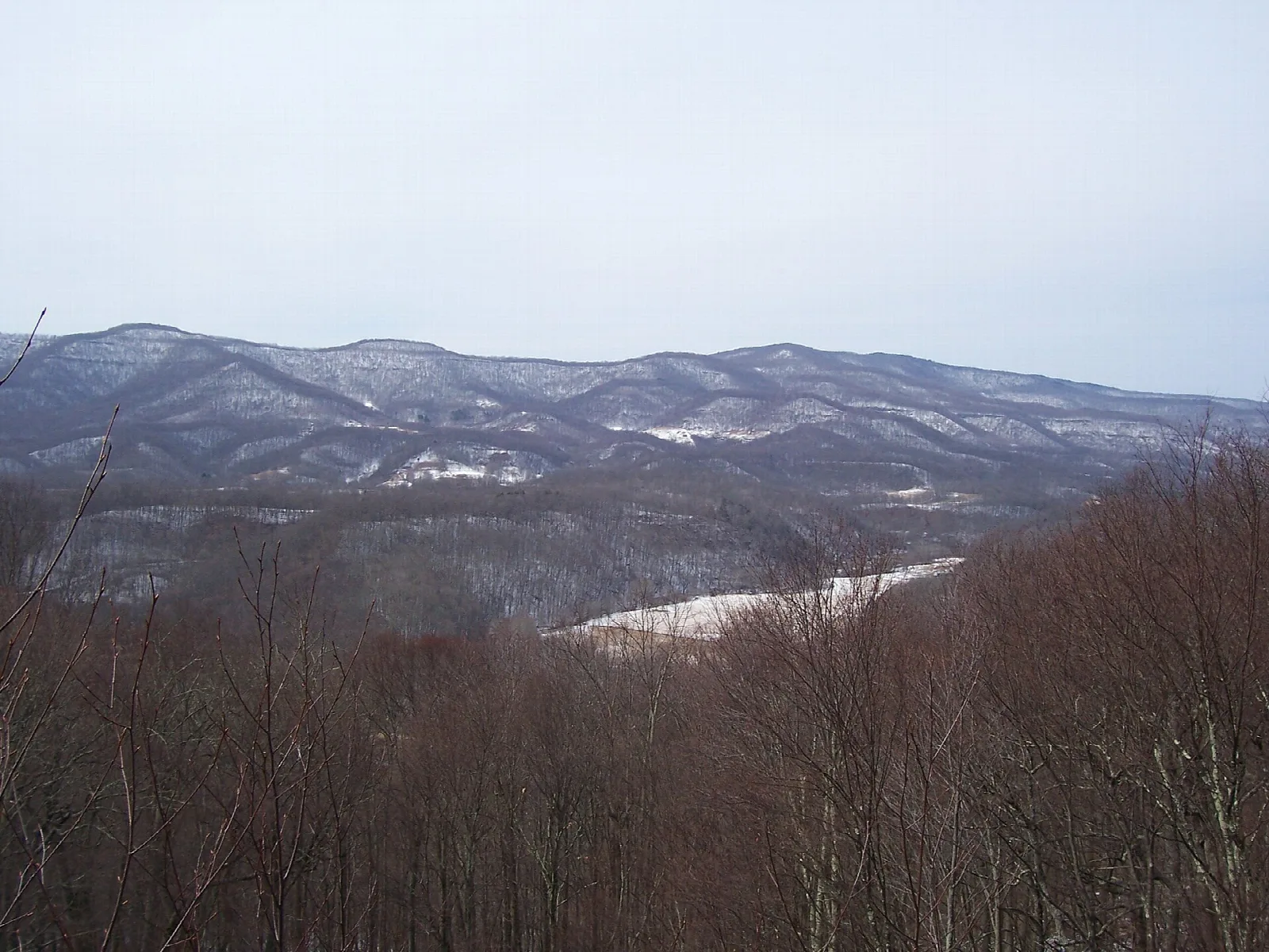 Winter view of forested ridges with patches of snow from an overlook