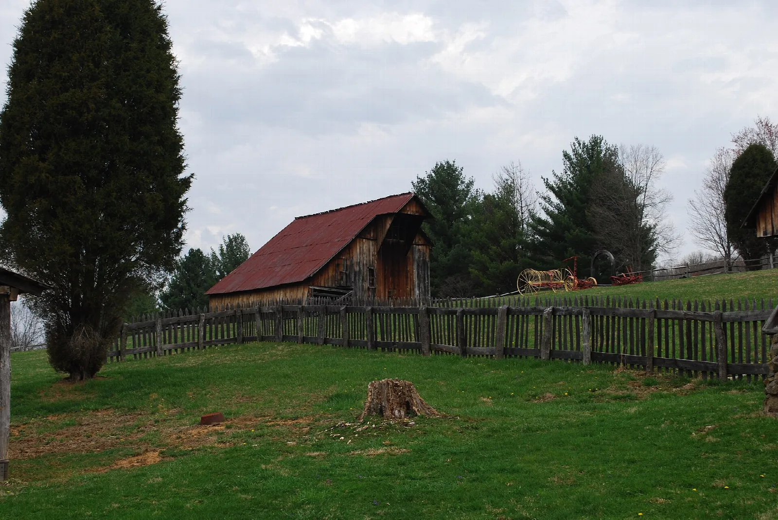 Wooden farm buildings with a red roof behind a split-rail fence on a green hill