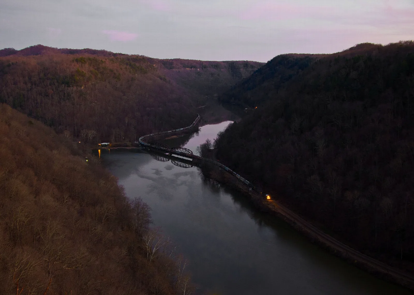 Dusky view down a river gorge with a rail bridge and red hillsides