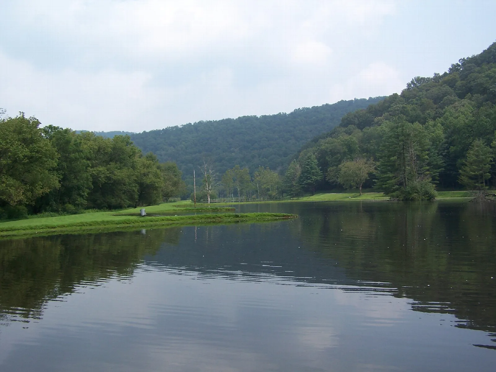 Calm lake reflecting green wooded hills under a cloudy sky