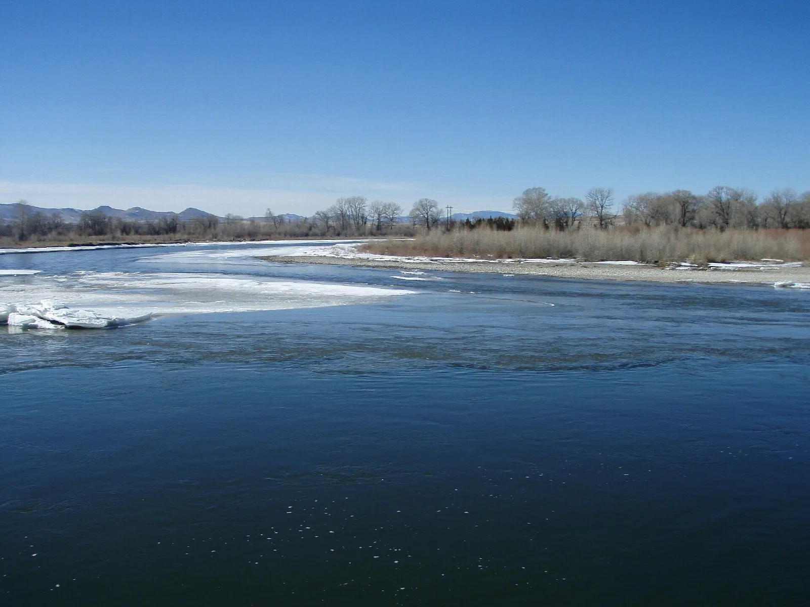 Wide river with ice along the bank under a clear blue sky