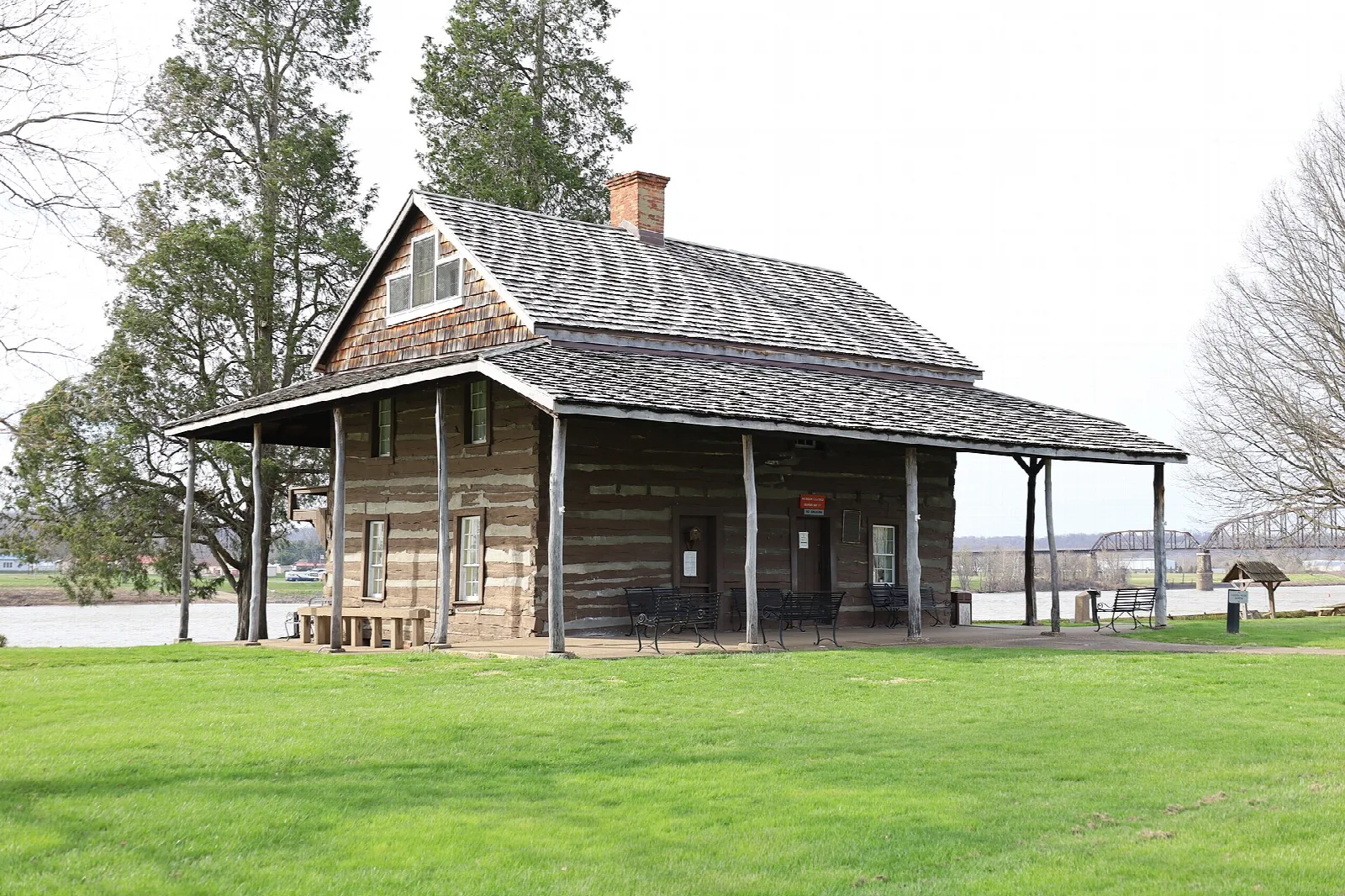 Log building with a covered porch on a green lawn near the river
