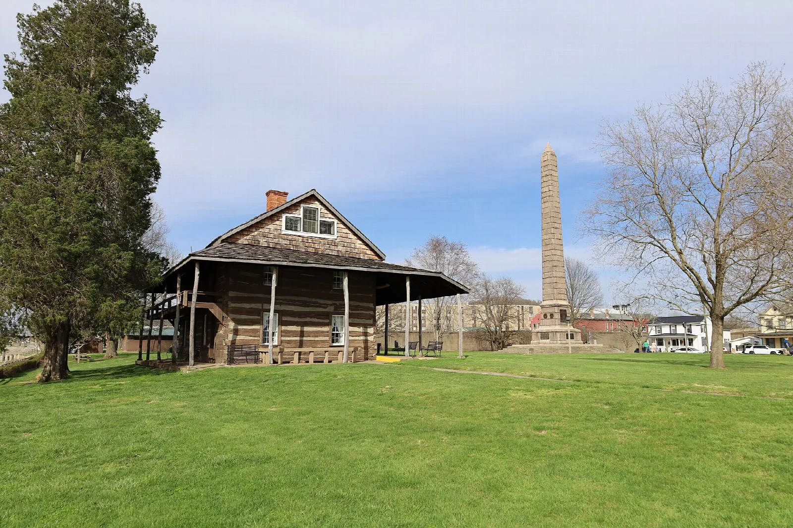 Log building with a porch on a lawn with a tall monument behind it