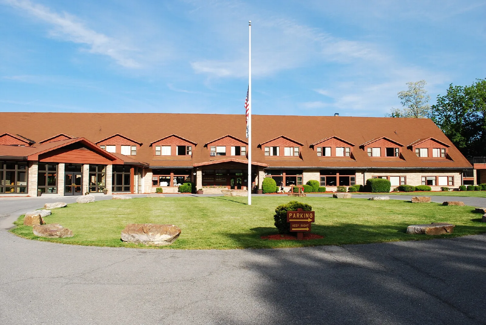 Long low lodge with a red roof and a flagpole on a lawn