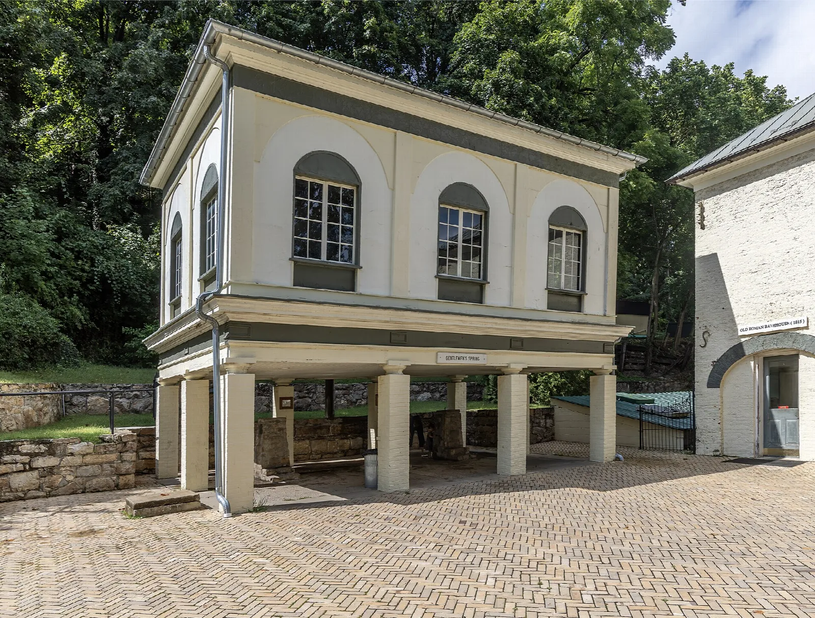Two-story cream bathhouse with arched windows and a brick patio