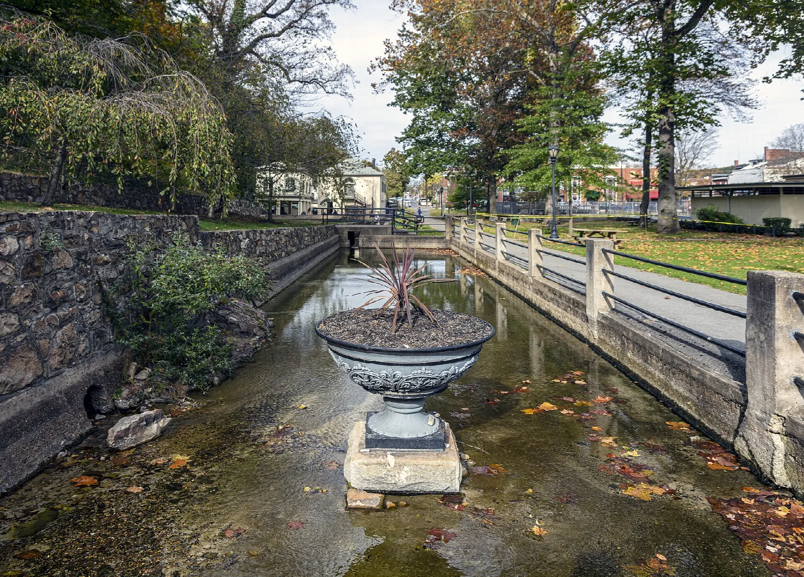 Stone-lined water channel with a stone urn and green trees