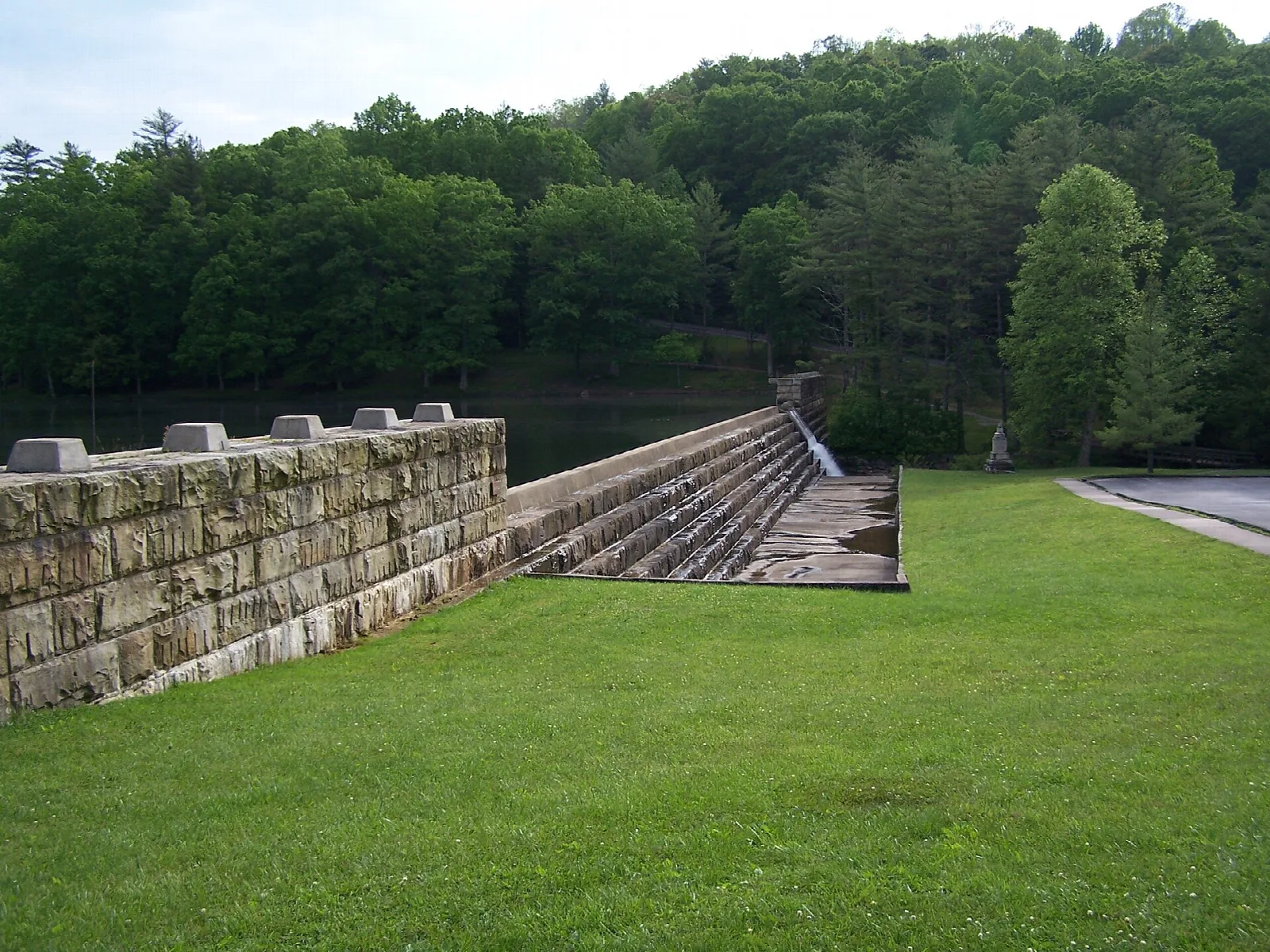 Stone dam wall beside a green lawn and trees