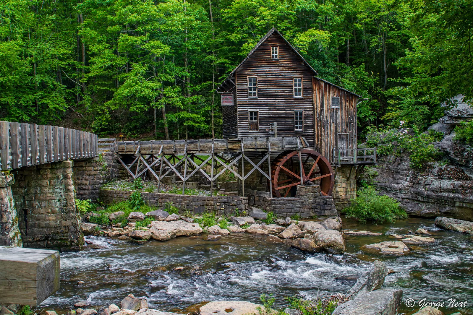 Grist mill with a red water wheel above a rocky creek in green forest