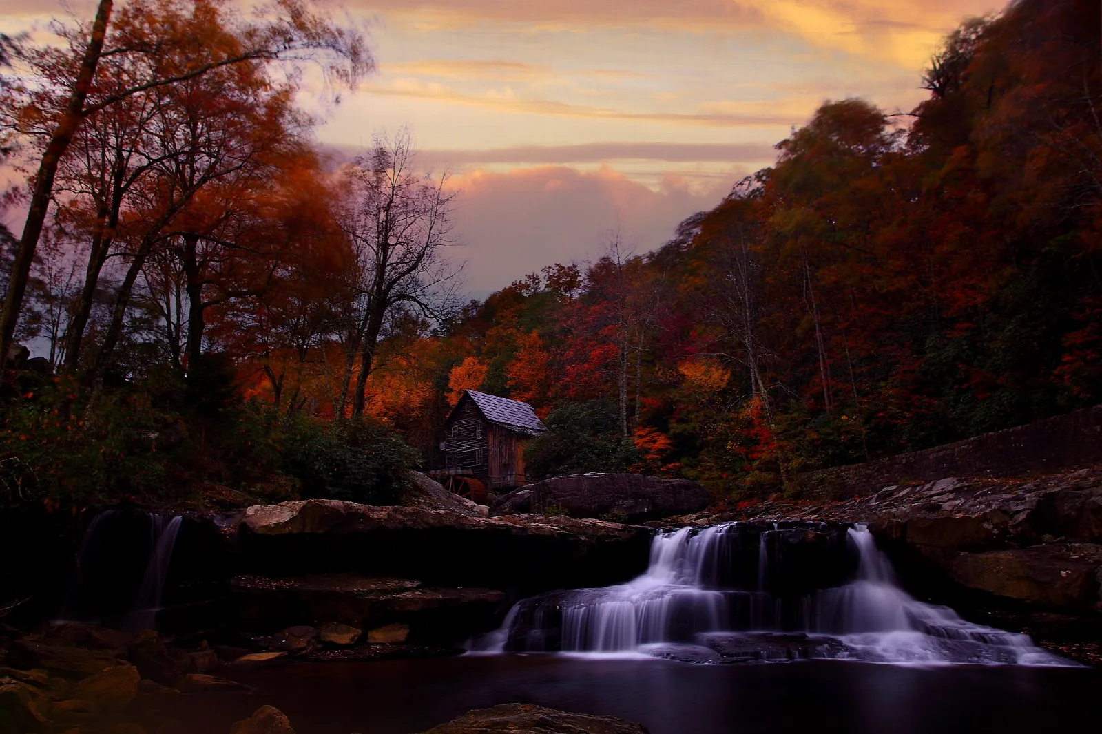Autumn forest and small waterfall at dusk with the mill in the distance