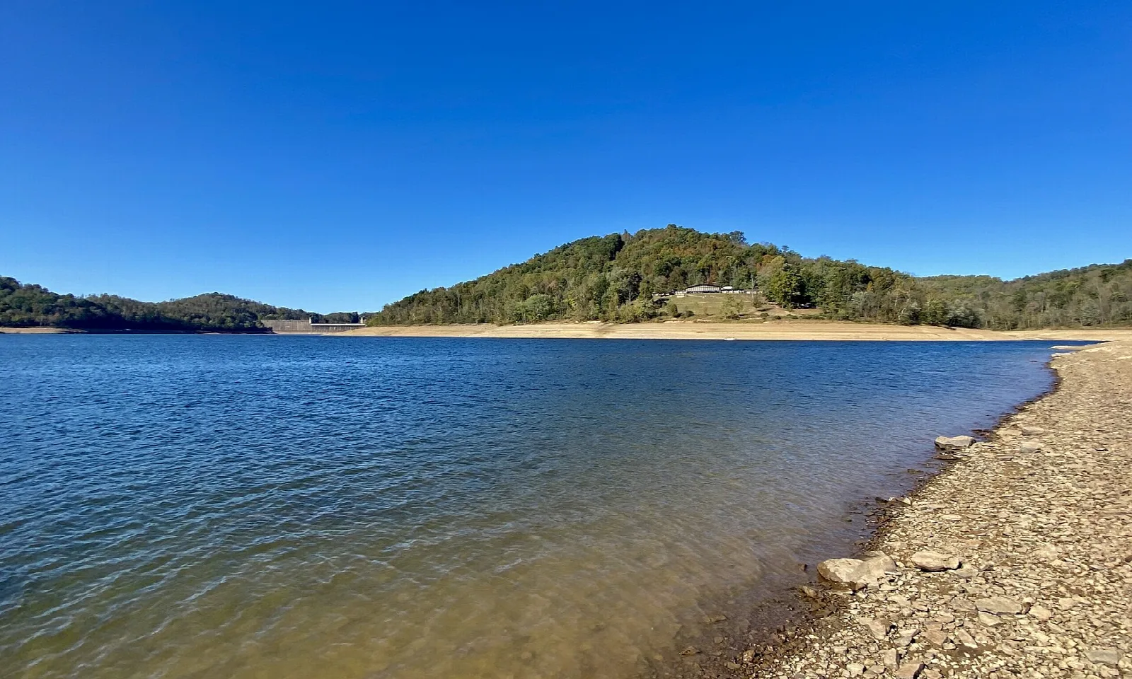 Blue lake with a stony shore and a forested hill across the water
