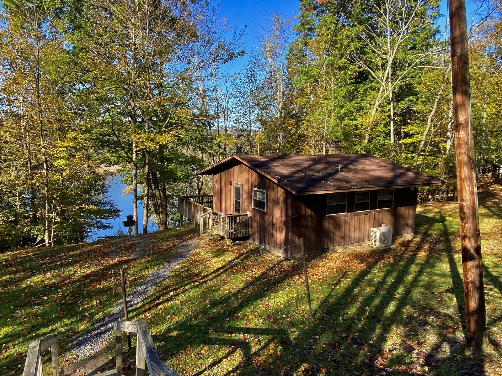 Brown lakeside cabin on a grassy slope among fall trees