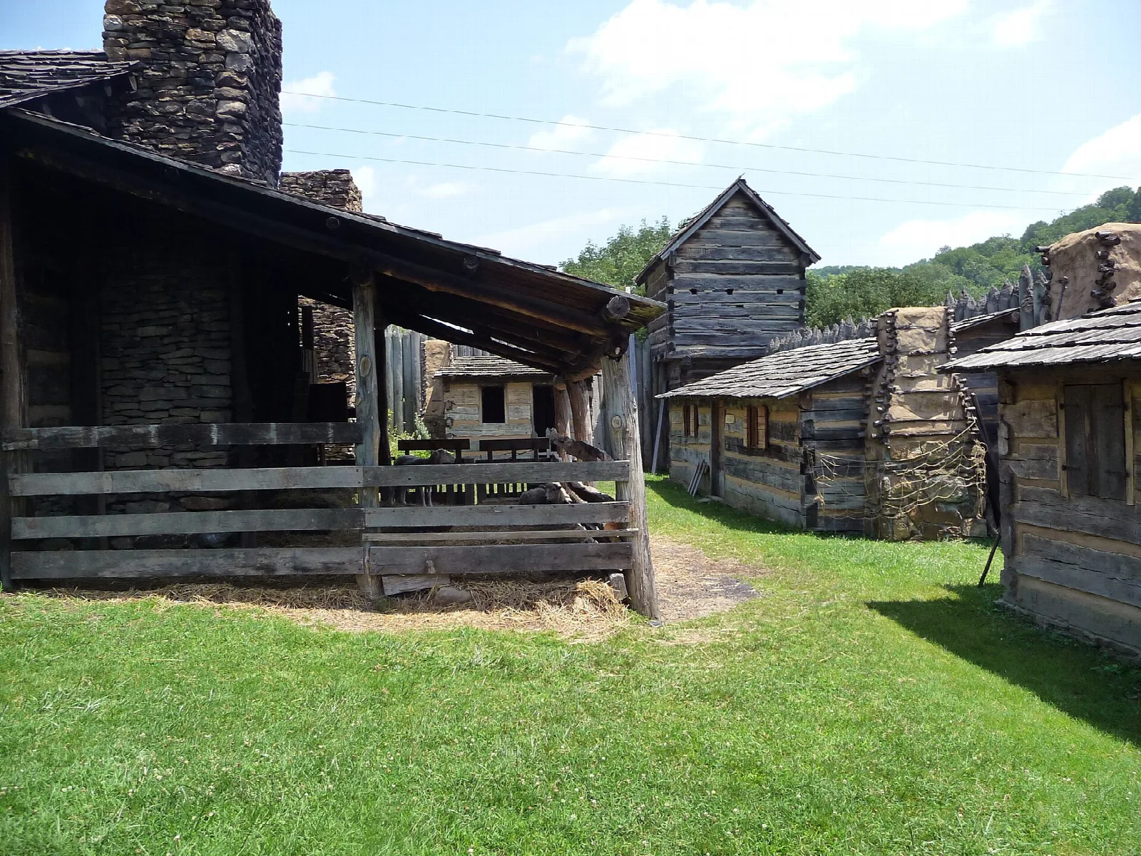 Log cabin with a stone chimney and porch beside the fort's other buildings