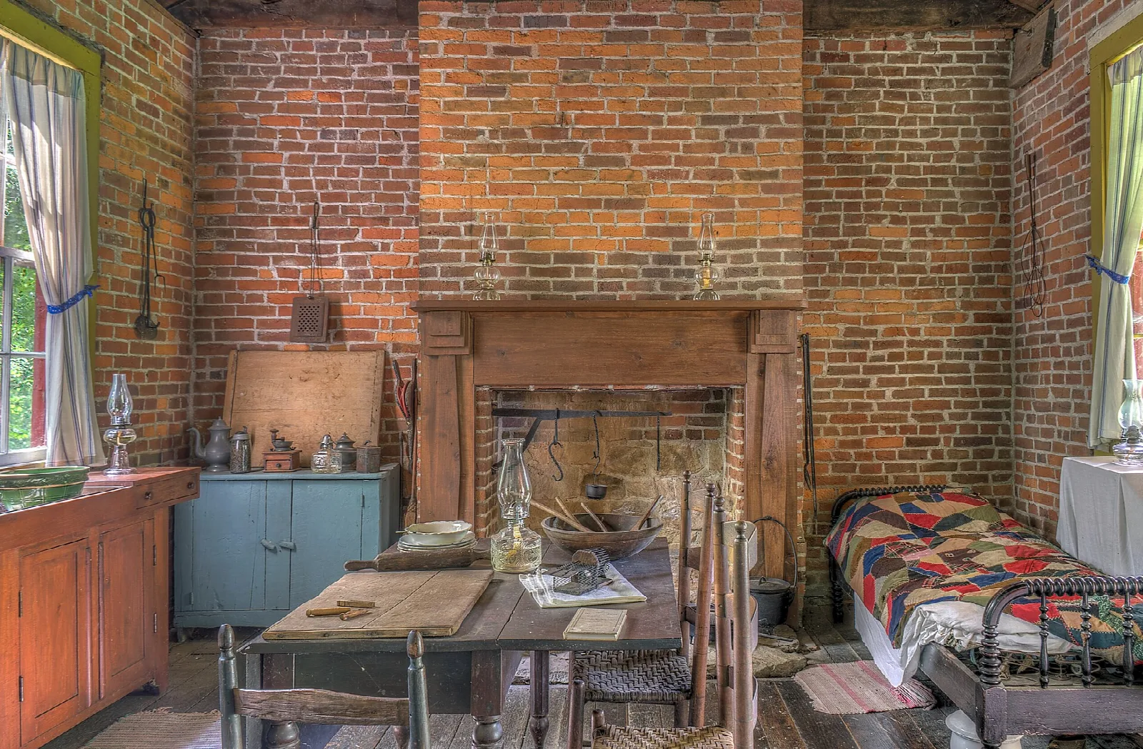 Old kitchen with a brick fireplace, a table, and a quilted bed