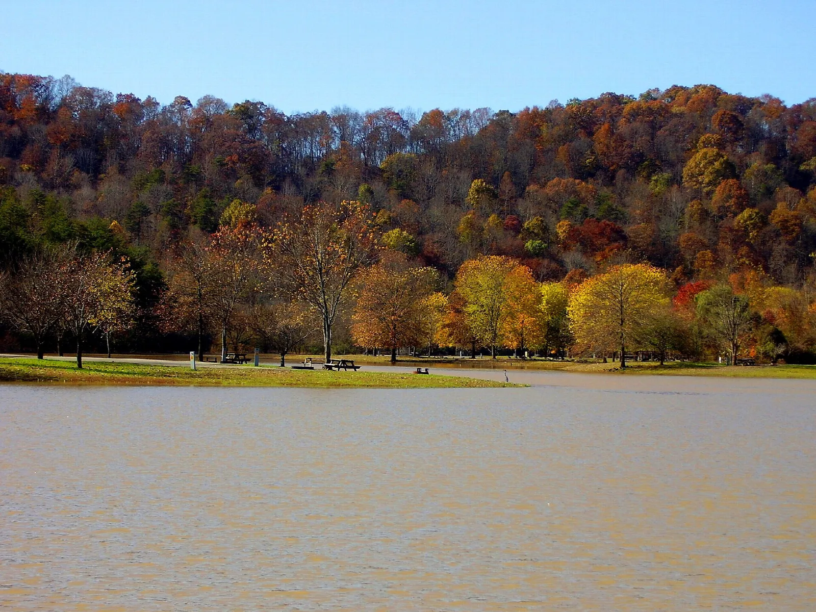 Calm lake in front of a hillside of orange and yellow fall trees