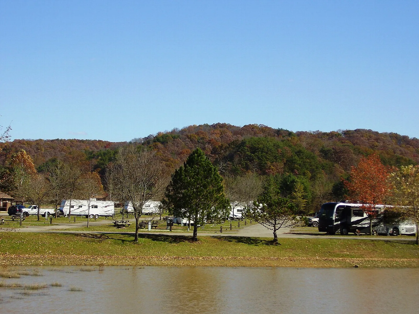 Campers and RVs on a grassy shore beside the lake under fall-colored hills