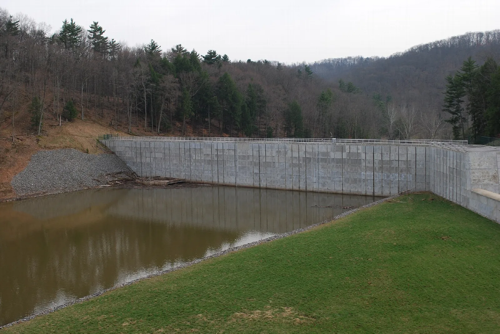 Concrete dam wall and a pool of water beside a grassy bank