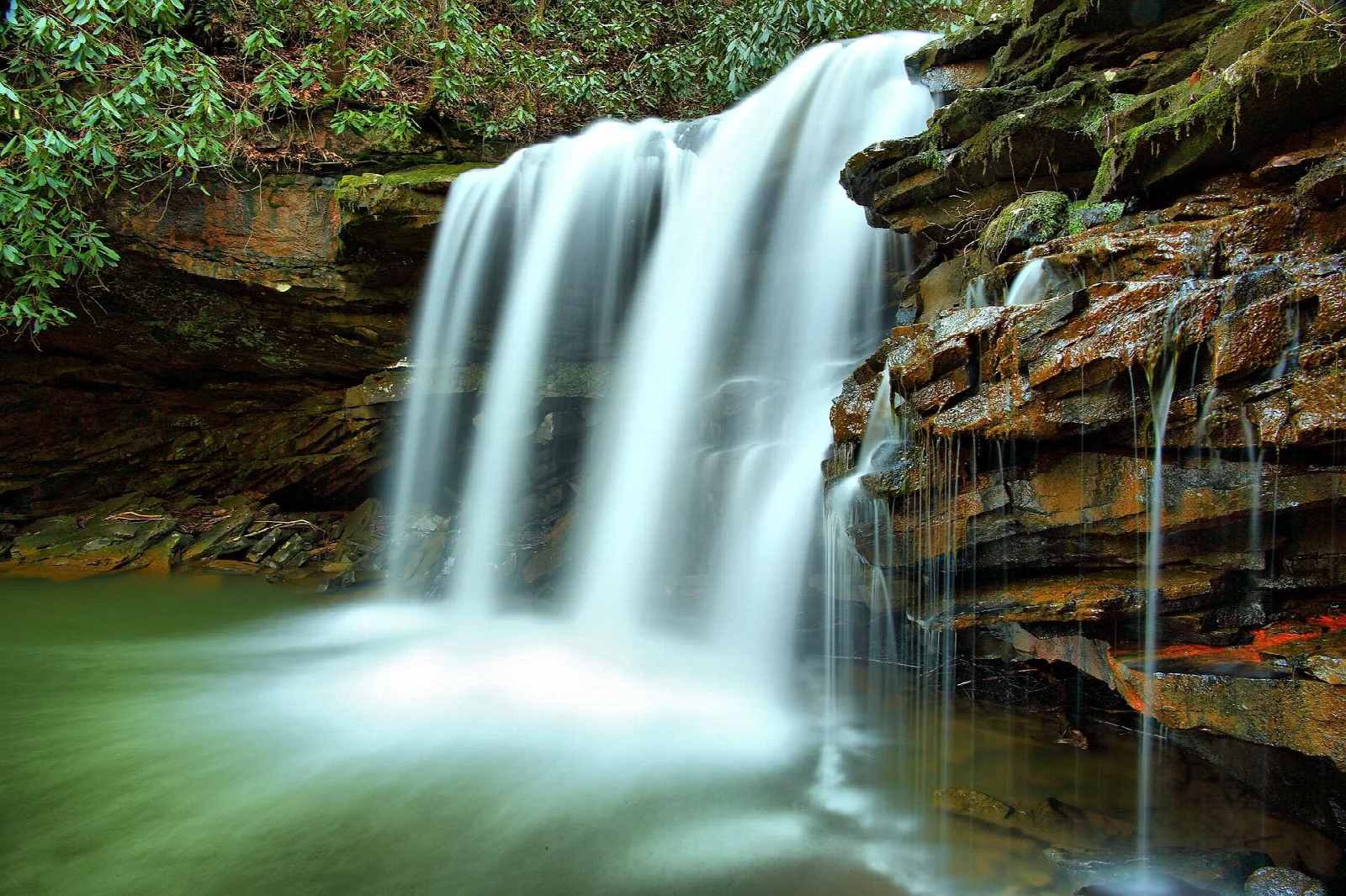 Tall waterfall dropping down a rock wall into a green pool