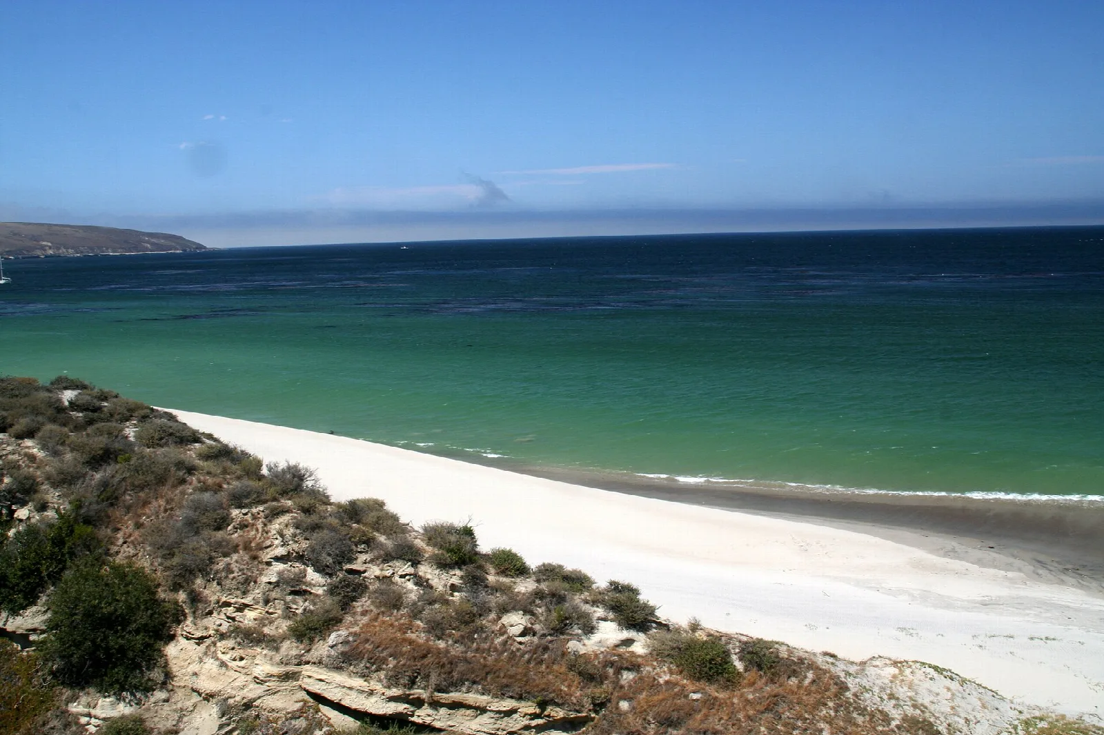 A curving white sand beach meeting turquoise water below scrubby hills