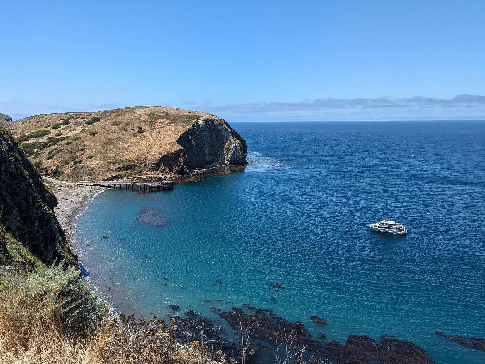 A sheltered cove of clear blue water below steep golden headlands