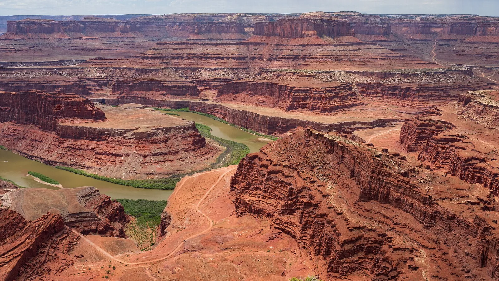 Layered red cliffs and a green river bend in a wide canyon