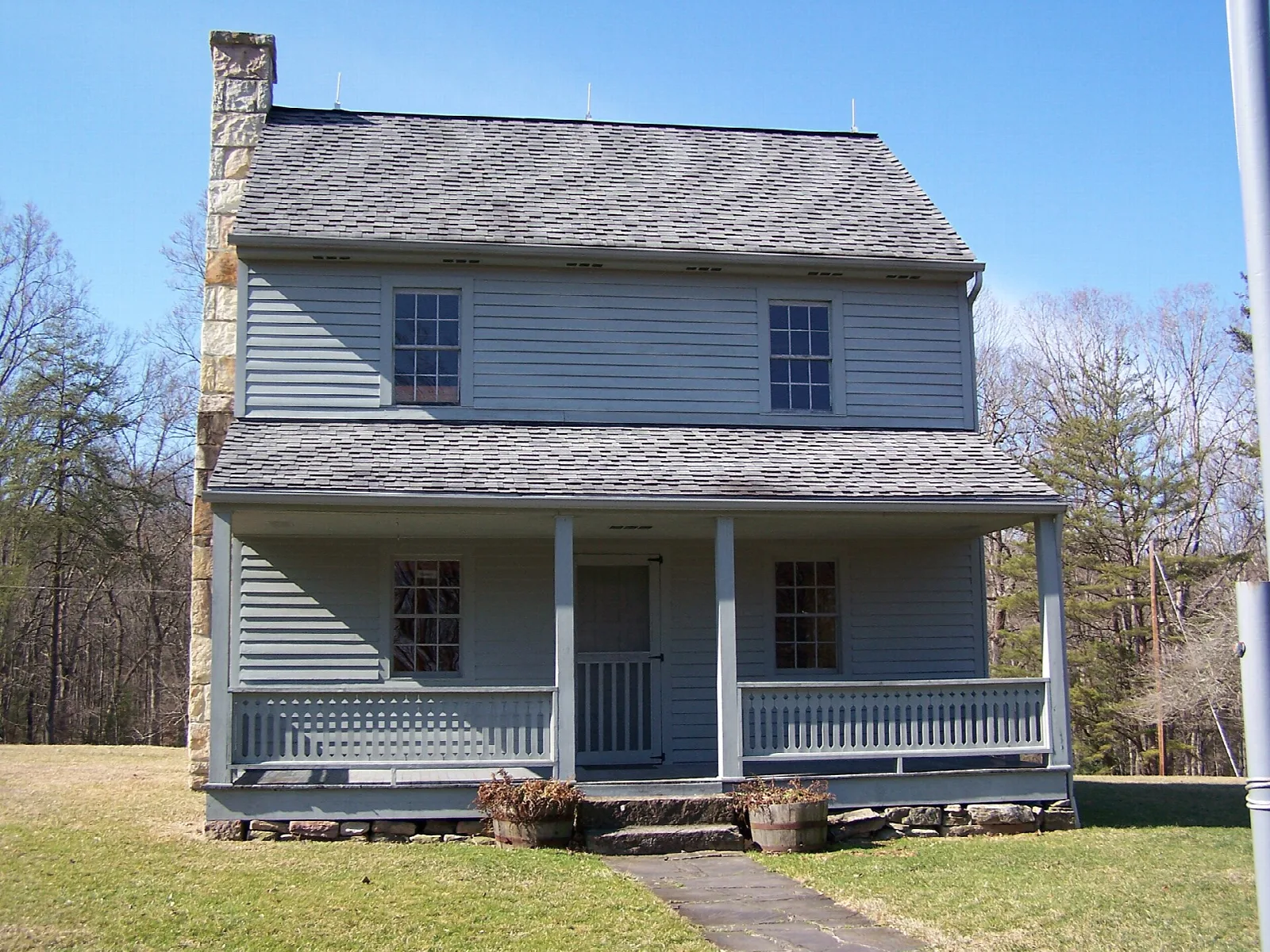 Two-story gray farmhouse with a front porch on a lawn under a blue sky
