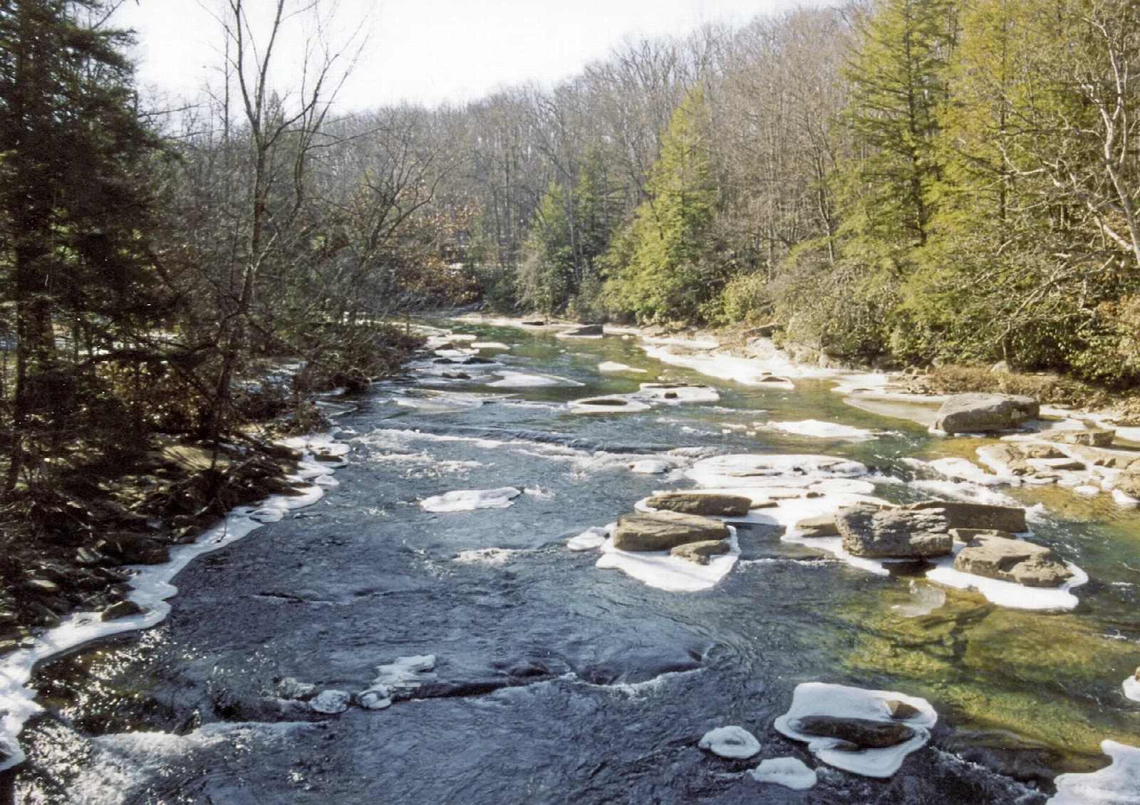River with ice along the banks running through bare winter woods