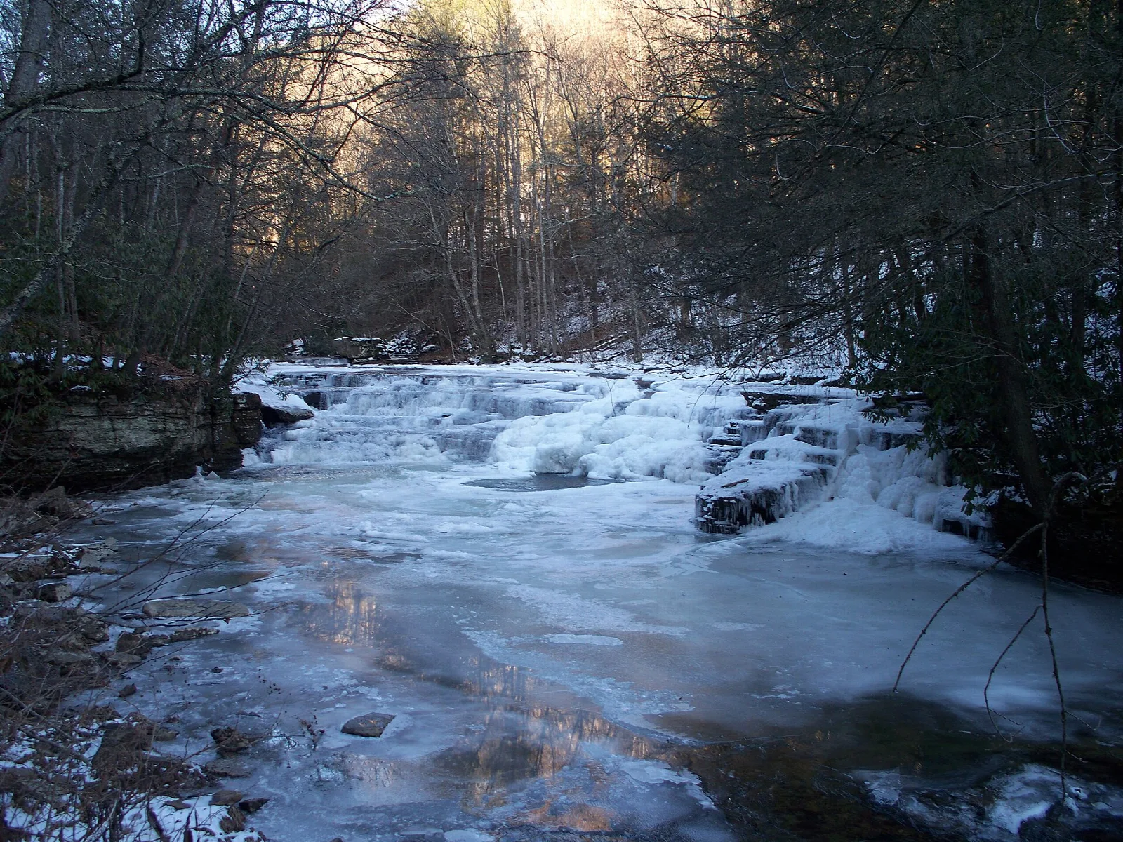 Frozen creek with ice over rock ledges in the woods