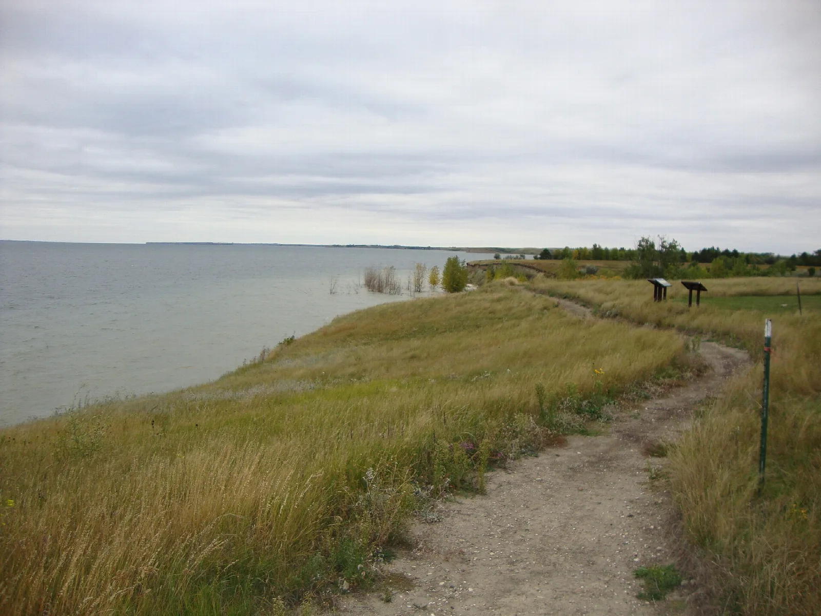Dirt path along a grassy bluff above the Lake Sakakawea shoreline under a cloudy sky