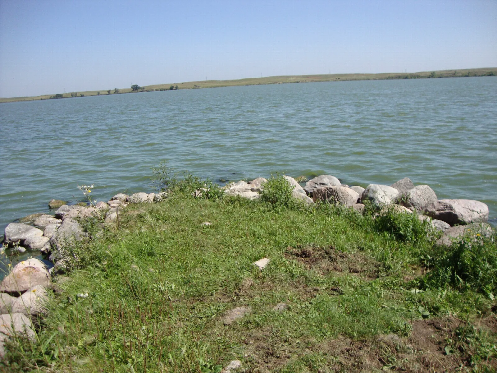 Grassy point edged with rocks reaching into a calm blue lake under a clear sky