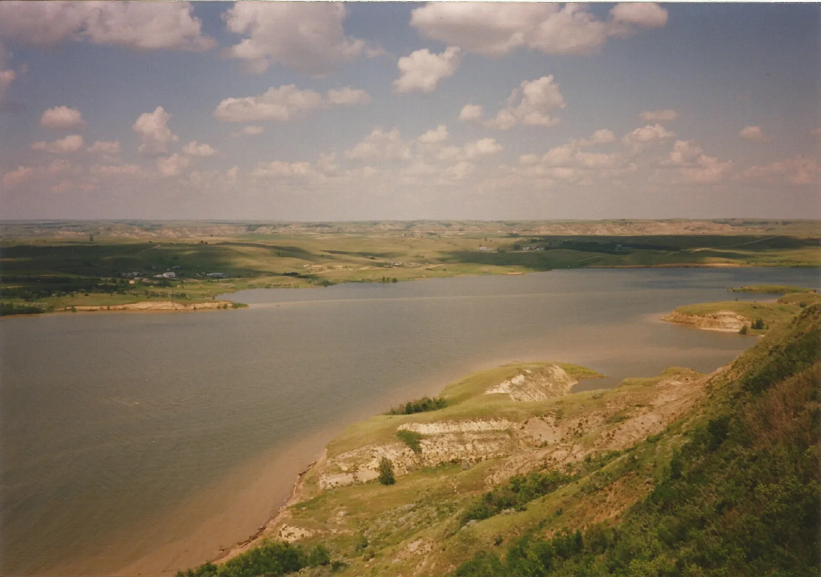 Wide view over Lake Sakakawea and green hills with bare cut banks under a cloudy sky