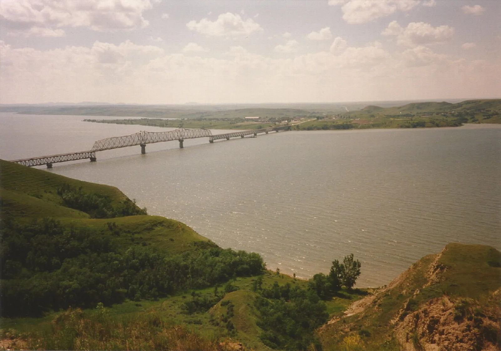 Old steel bridge crossing a wide lake below green grassy hills