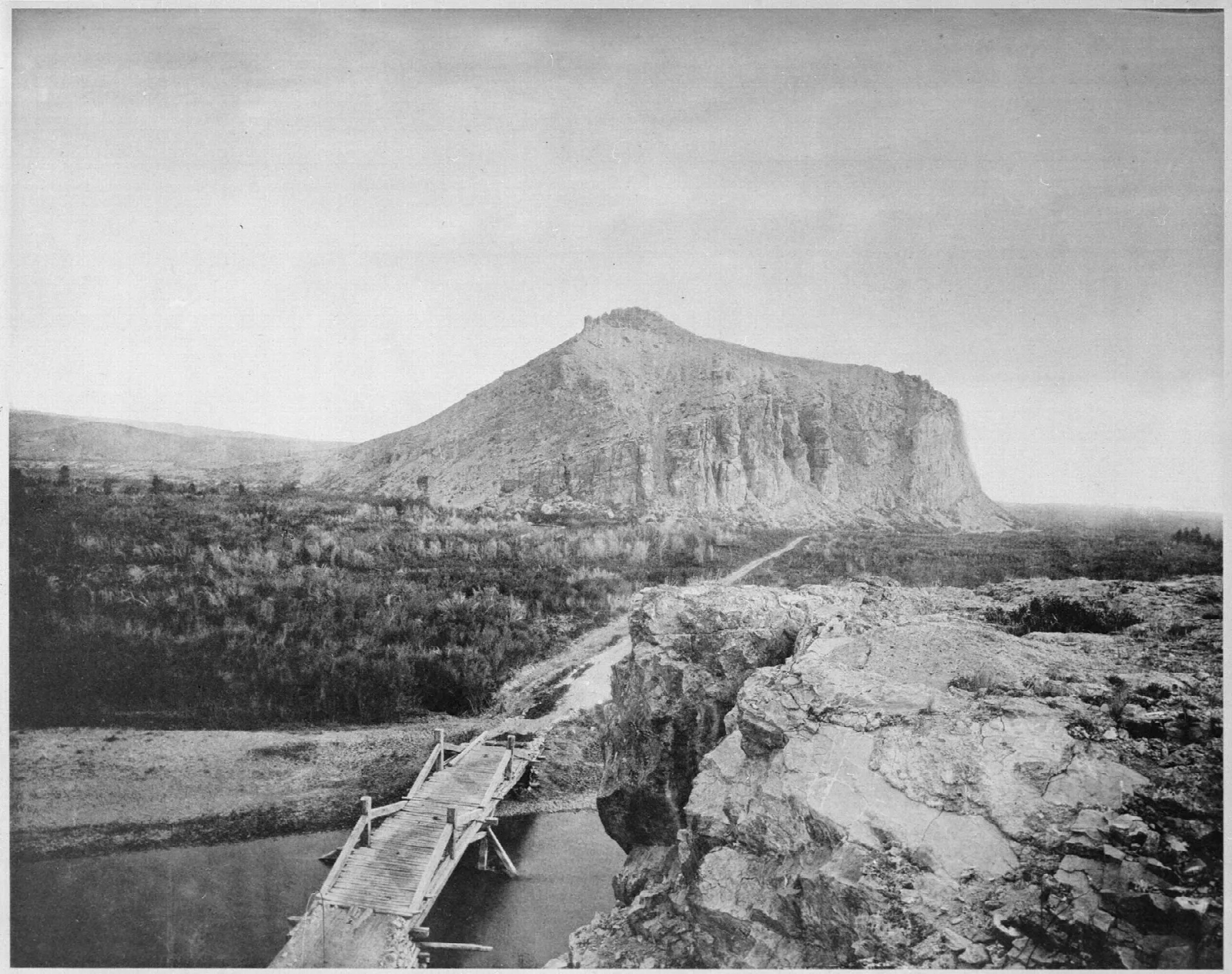 Old black and white photo of a flat-topped rock bluff above a river
