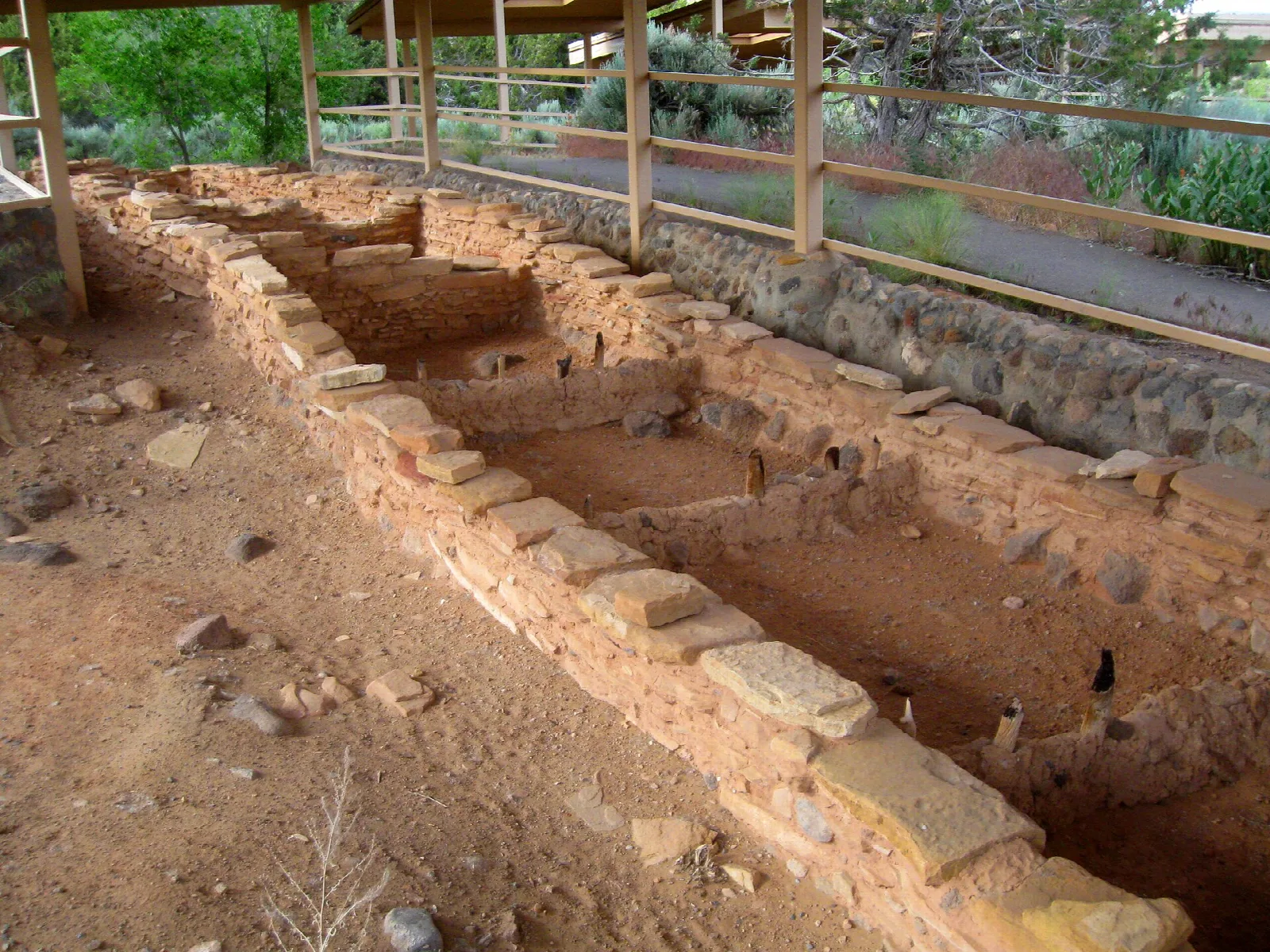 Low stone walls of excavated rooms with a roof overhead
