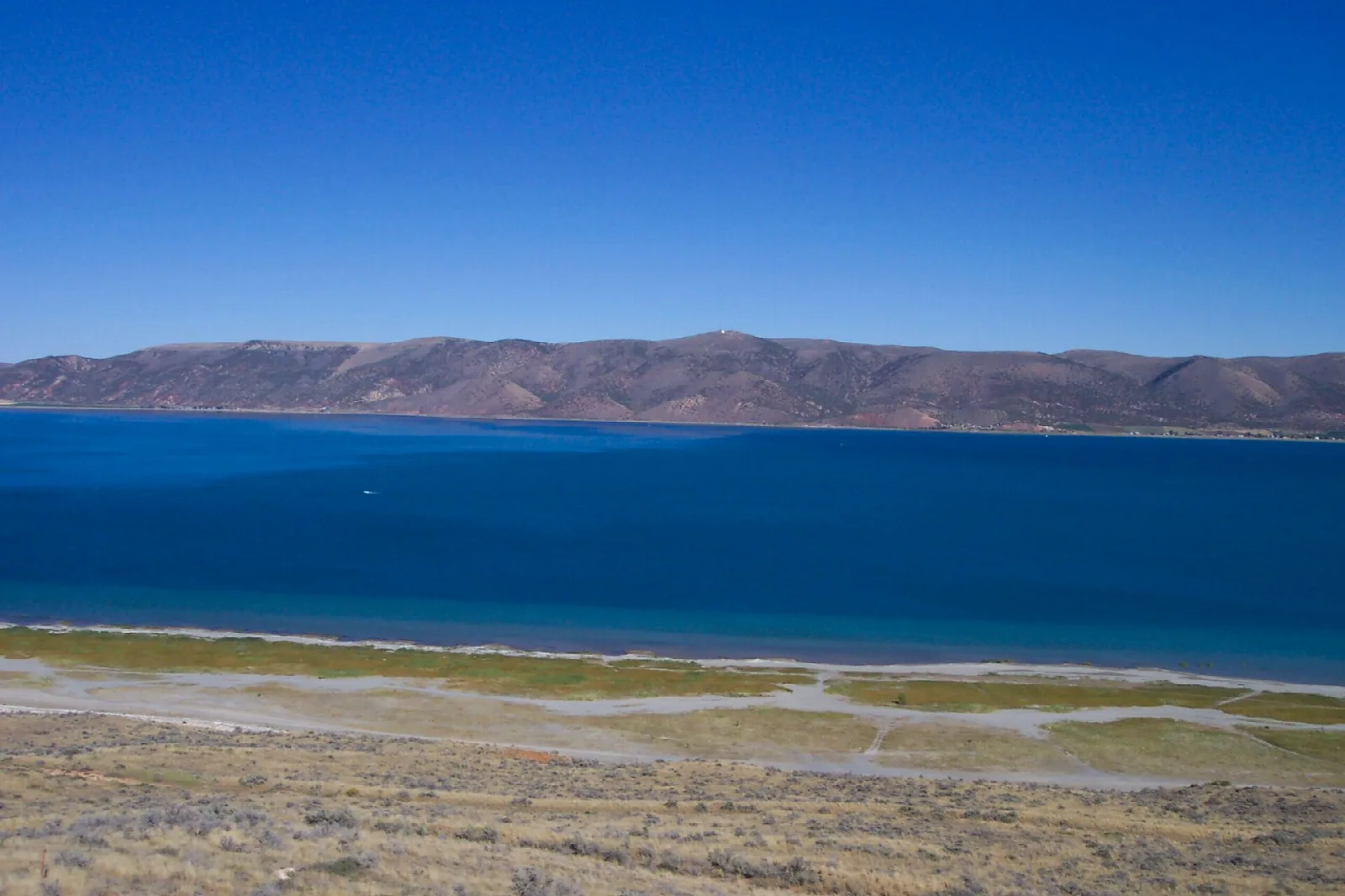 Deep blue lake below a low mountain ridge with a grassy shoreline
