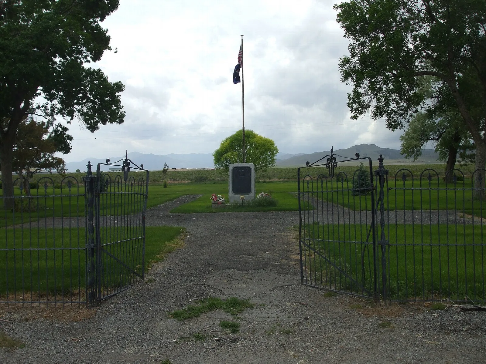 Iron gates leading to a small cemetery with a flagpole and monument