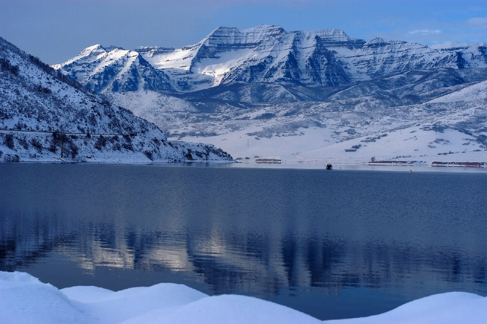 Snow-covered mountain reflected in the calm blue water of a reservoir