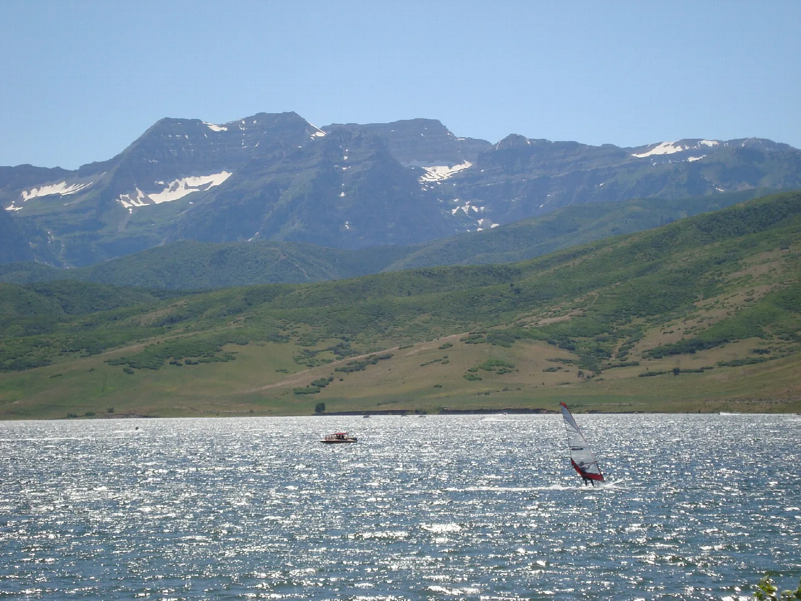 Sparkling reservoir water with a green mountain slope and distant sailboats