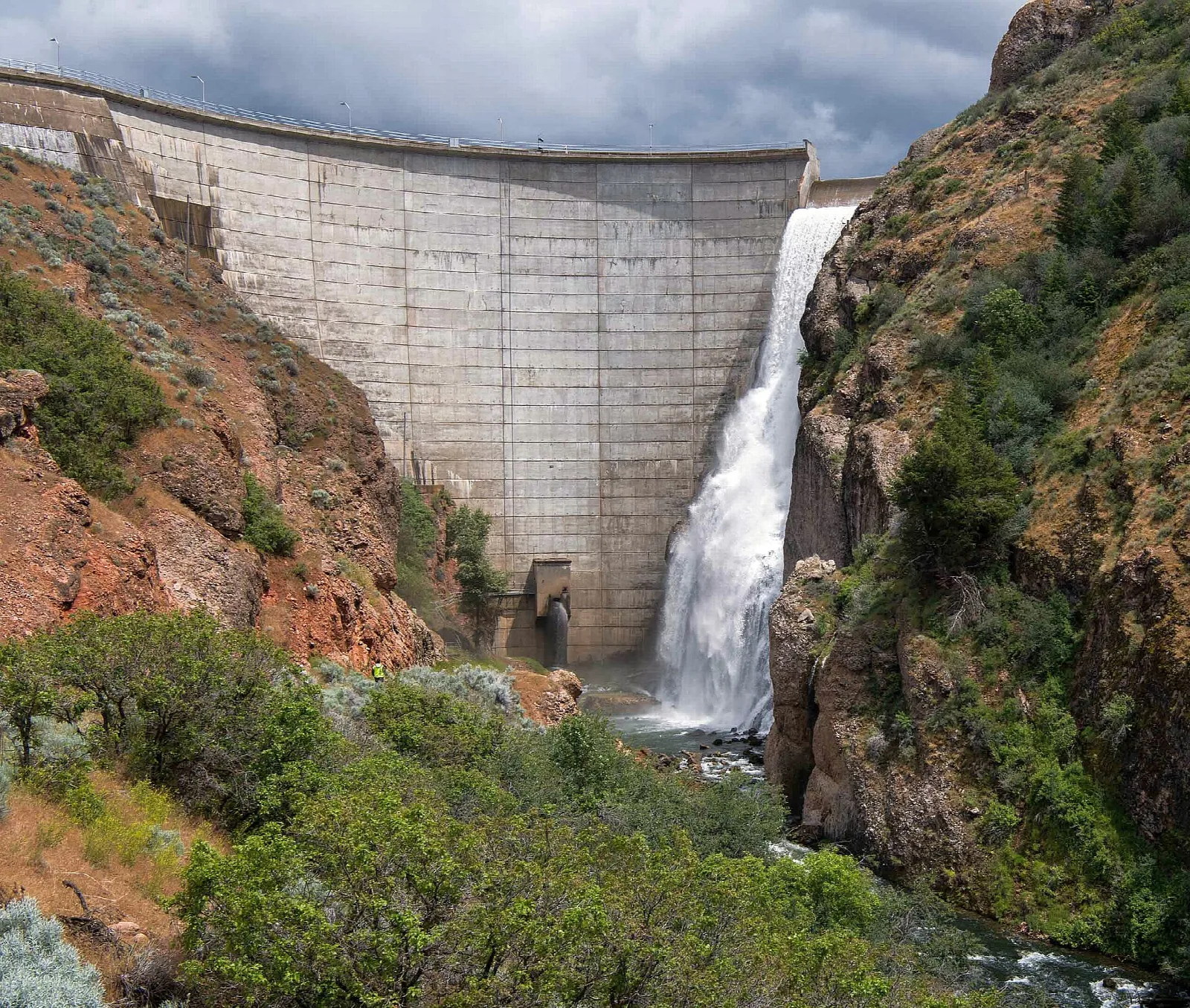 Concrete dam with water spilling down a rocky canyon wall