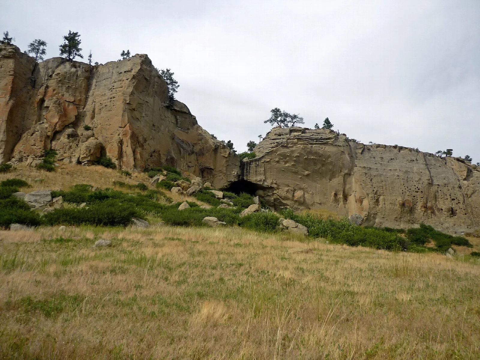 Sandstone cliffs above a grassy hillside under a cloudy sky
