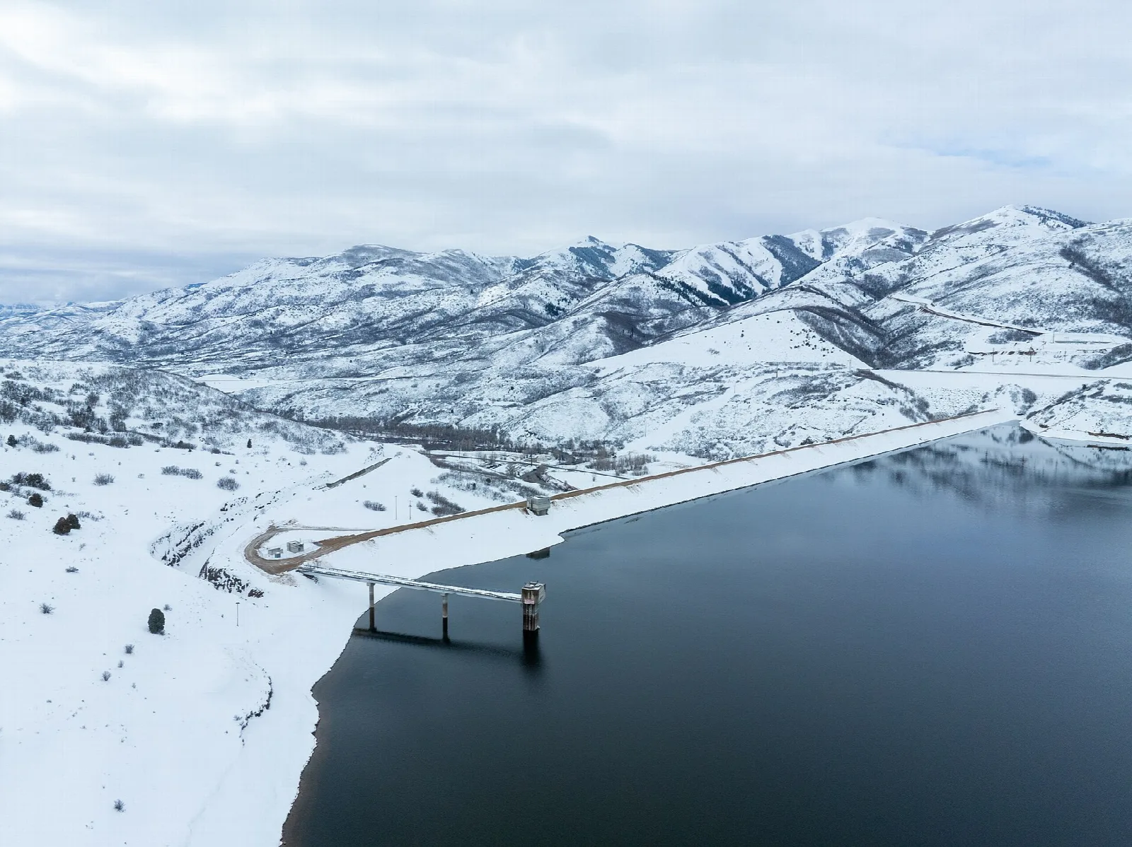 Snowy hills and a dark reservoir seen from an overlook, with the dam curving along the shore