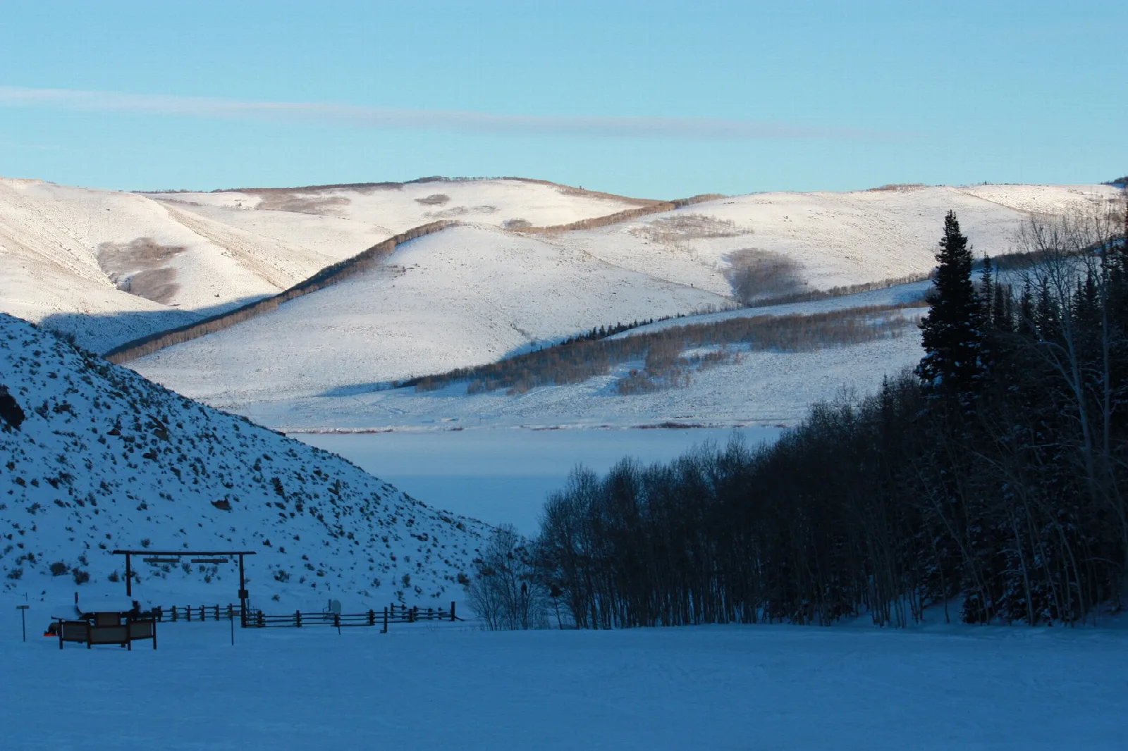 Snow-covered hills and a frozen reservoir with a fenced area in the foreground