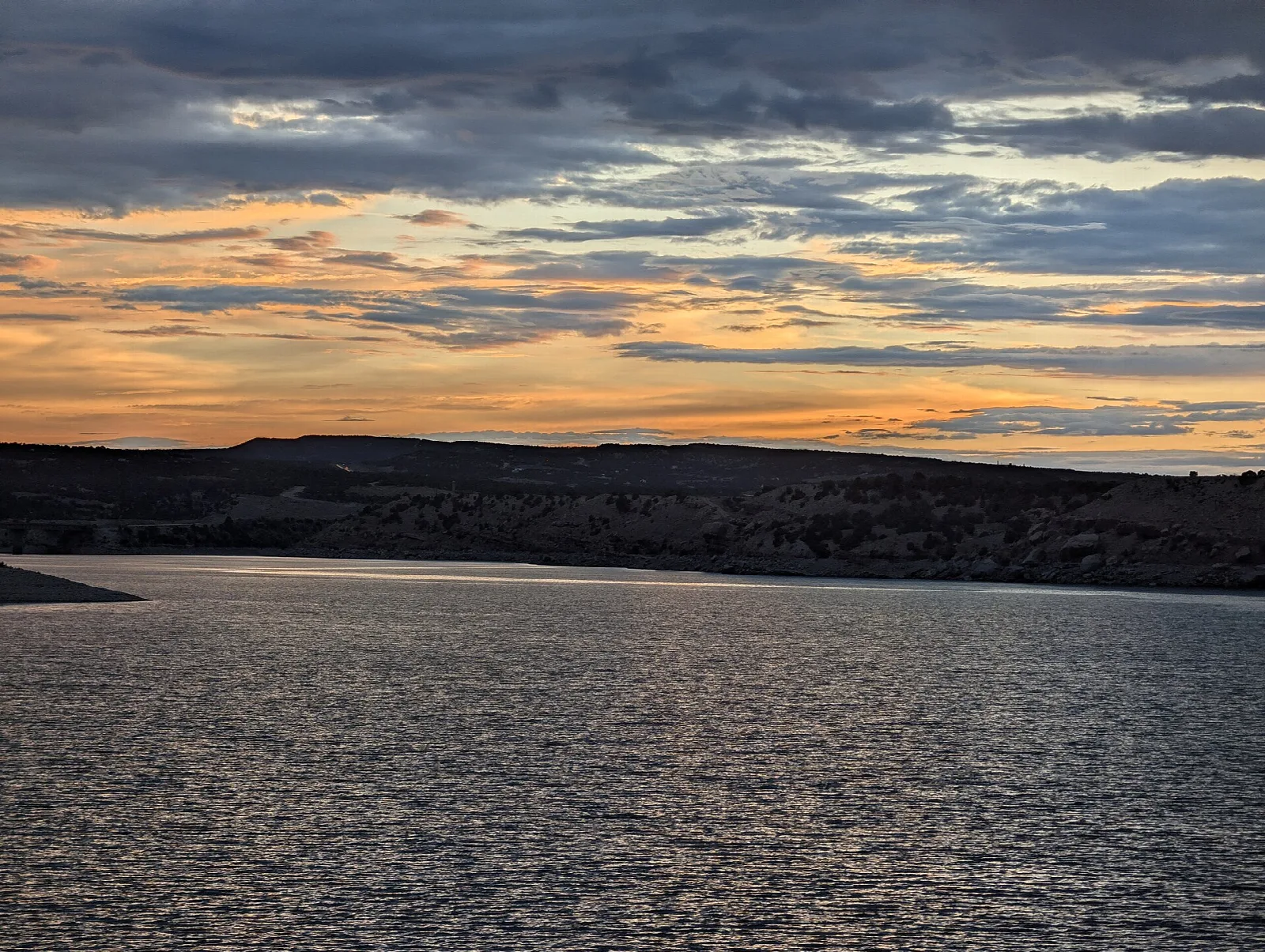 Orange sunset sky over a wide reservoir and dark hills